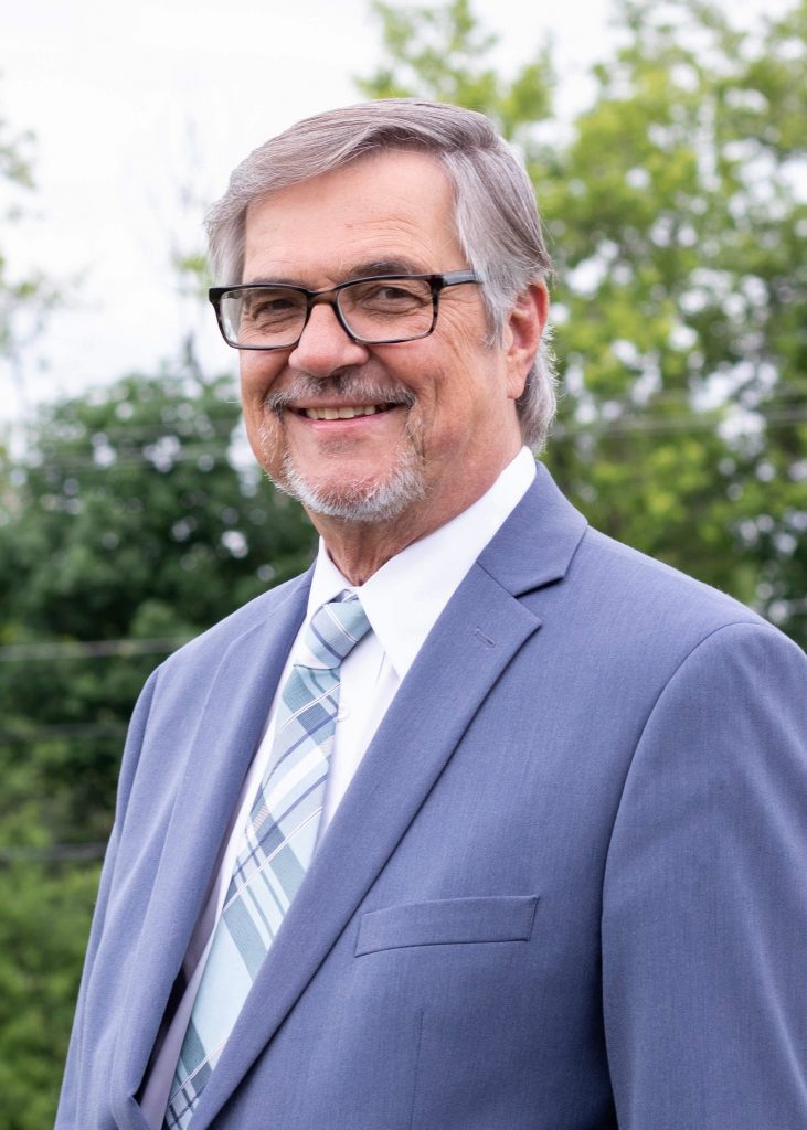 A man wearing a blue suit jacket smiles at the camera.